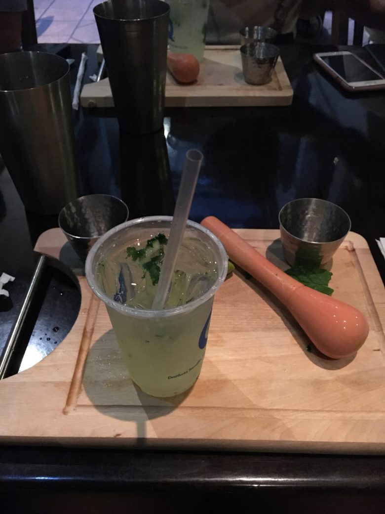A green alcoholic drink, freshly made on a chopping board with pestle beside in it, in post titled #SoSS