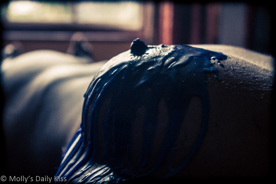 A shot down the line of Cara's body with her blue wax covered breast in the foreground